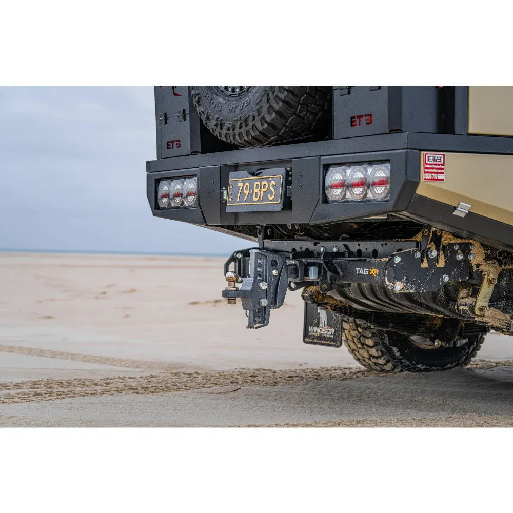 Close-up of a vehicle's hitch and trailer tow setup on a sandy surface.